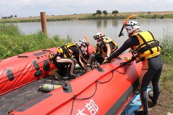 潜水装備をつけ、高機能救命ボートとともに川に入る隊員の写真