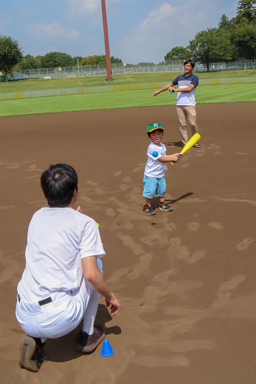 おとうさんの前でバットを振る子どもの写真