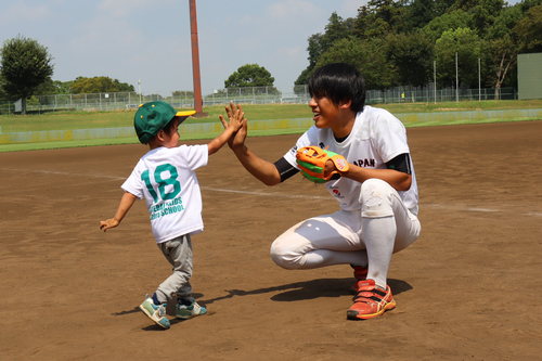 お兄さんとハイタッチをするユニフォームを着た子どもの写真